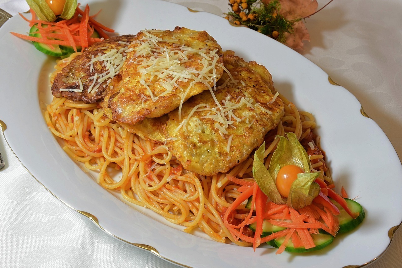 Ein Teller Spaghetti mit Käse, frittierten Schnitzeln und frischem Gemüse, serviert auf einem eleganten weißen Geschirr.