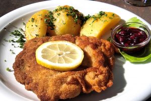 Ein knuspriges Schnitzel mit Zitrone, Kartoffeln und Preiselbeersoße auf einem Teller, garniert mit frischen Kräutern.
