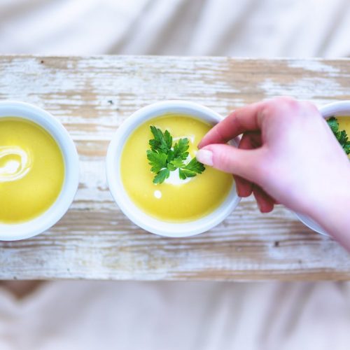 Drei Schalen mit cremiger Kartoffelsuppe, garniert mit frischer Petersilie und einem Spritzer Sahne.