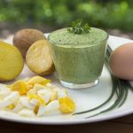 Ein Teller mit gekochten Eiern, Kartoffeln und einer grünen Kräutersauce, die frische Zutaten zeigt.