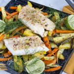 Gebackener Fischfilet auf einem Blech mit buntem Gemüse, darunter Karotten und Kartoffeln, garniert mit Limetten und Dill.