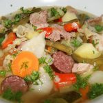 Eine herzhafte Gemüsesuppe mit Fleisch, Karotten, Kartoffeln und frischen Kräutern in einer weißen Schüssel.