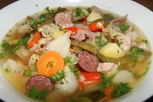 Eine herzhafte Gemüsesuppe mit Fleisch, Karotten, Kartoffeln und frischen Kräutern in einer weißen Schüssel.