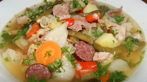 Eine herzhafte Gemüsesuppe mit Fleisch, Karotten, Kartoffeln und frischen Kräutern in einer weißen Schüssel.