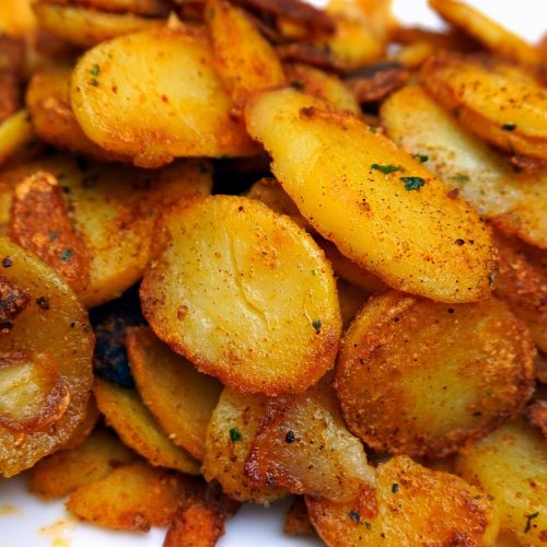 Würzige gebratene Kartoffelscheiben mit Gewürzen und Kräutern, knusprig und goldbraun, ideal für Beilagen oder Snacks.