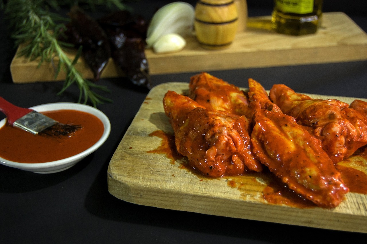 Würzige Hähnchenflügel auf einem Holzbrett mit roter Sauce, umgeben von Zutaten wie Knoblauch und Olivenöl.