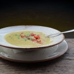 Kremige Gemüsesuppe in einer weißen Schüssel mit frischen Kräutern und Paprika, serviert auf einem Holzuntergrund.