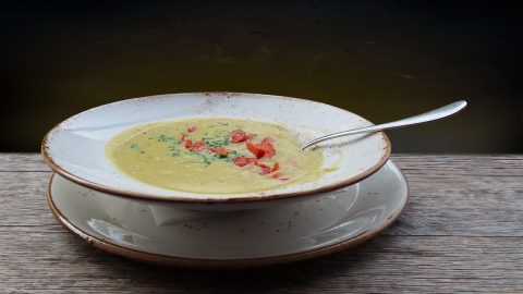 Kremige Gemüsesuppe in einer weißen Schüssel mit frischen Kräutern und Paprika, serviert auf einem Holzuntergrund.