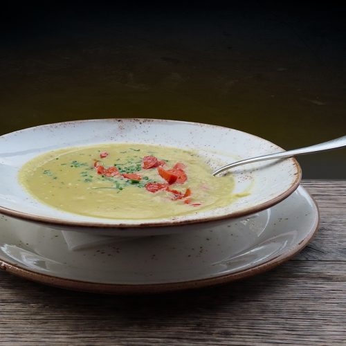Kremige Gemüsesuppe in einer weißen Schüssel mit frischen Kräutern und Paprika, serviert auf einem Holzuntergrund.