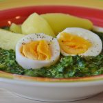 Ein Teller mit Spinat, gekochten Eiern und Kartoffeln, serviert in einer bunten Schüssel. Gesundes und nahrhaftes Gericht.