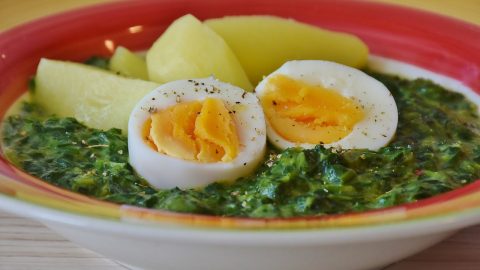 Ein Teller mit Spinat, gekochten Eiern und Kartoffeln, serviert in einer bunten Schüssel. Gesundes und nahrhaftes Gericht.