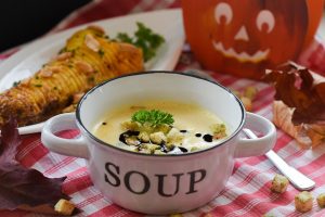 Schüssel mit Blumenkohlsuppe, garniert mit Croutons und Petersilie, auf einem karierten Tisch. Herbstliche Dekoration im Hintergrund.