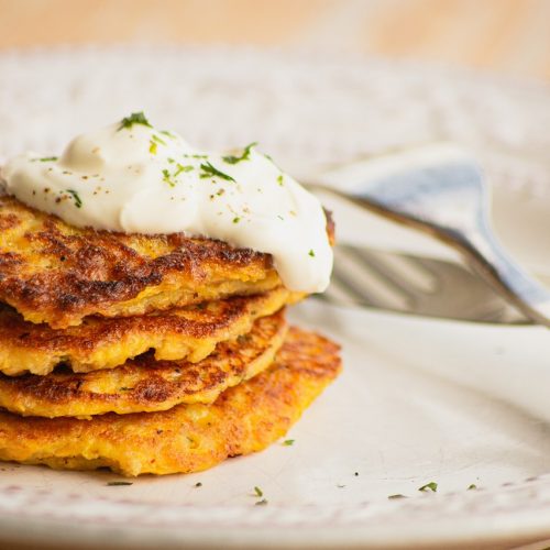 Leckere Kartoffelpuffer gestapelt mit einem Klecks Sauerrahm, serviert auf einem weißen Teller, ideal für ein herzhaftes Gericht.