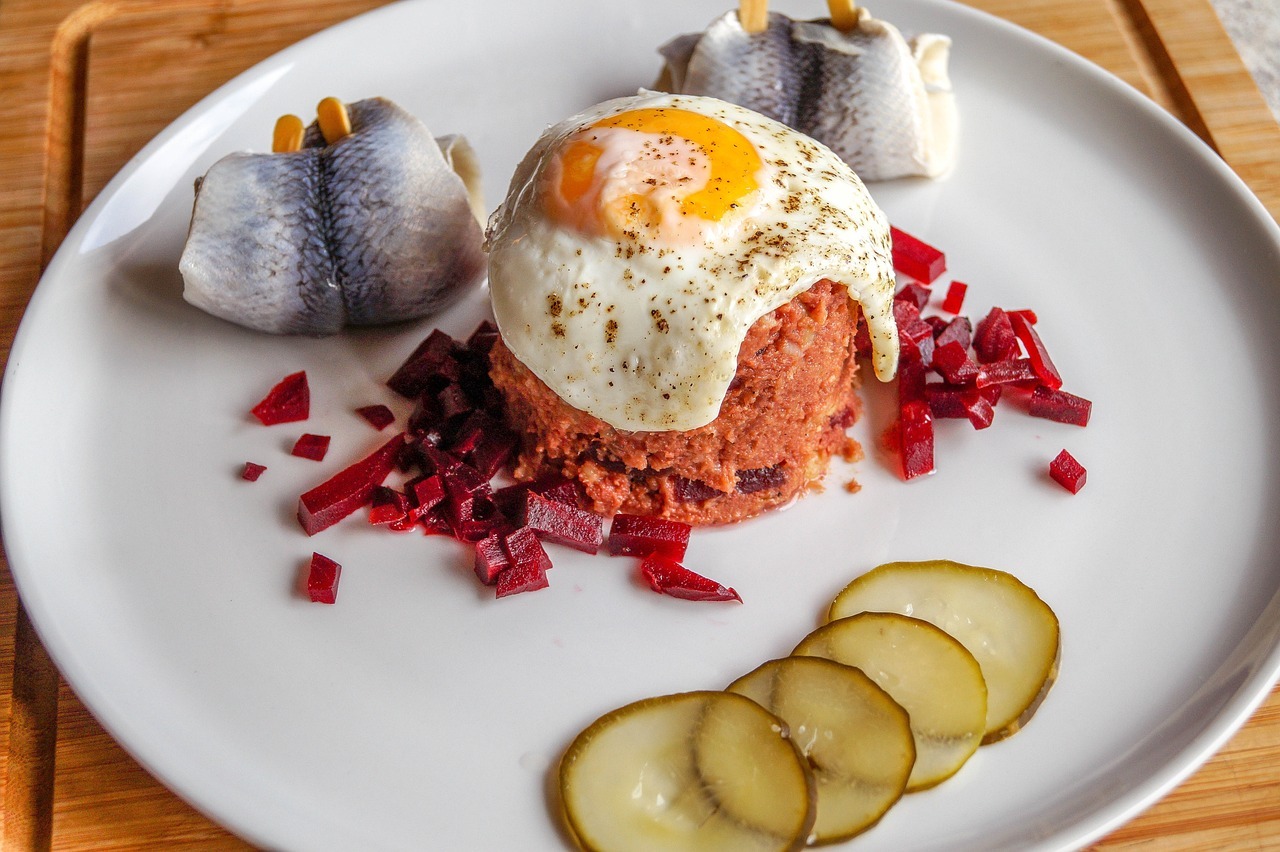 Ein Teller Labskaus, ein Gericht aus Rinderhack, einem Spiegelei, eingelegten Gurken und Fischfilets auf einem weißen Teller.