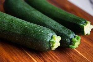Drei frische grüne Zucchini auf einem Holzbrett, ideal für gesunde Rezepte und Kochideen, reich an Nährstoffen und Vitaminen.