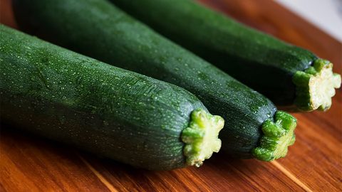 Drei frische grüne Zucchini auf einem Holzbrett, ideal für gesunde Rezepte und Kochideen, reich an Nährstoffen und Vitaminen.
