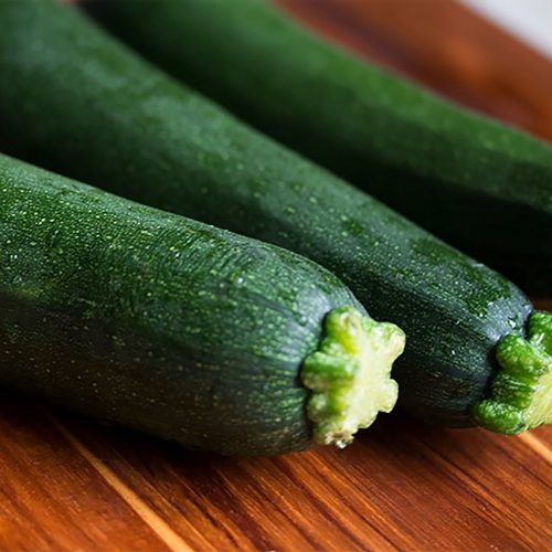 Drei frische grüne Zucchini auf einem Holzbrett, ideal für gesunde Rezepte und Kochideen, reich an Nährstoffen und Vitaminen.