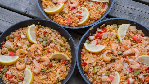Drei Pfannen mit Meeresfrüchte-Paella, garniert mit Zitronenscheiben und buntem Gemüse, ideal für Feinschmecker und Liebhaber der mediterranen Küche.