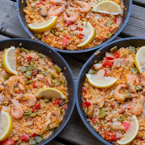 Drei Pfannen mit Meeresfrüchte-Paella, garniert mit Zitronenscheiben und buntem Gemüse, ideal für Feinschmecker und Liebhaber der mediterranen Küche.
