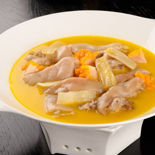 Hühnerflügel in einer gelben Brühe mit Karotten und Sellerie, serviert in einer weißen Schüssel auf einem dunklen Tisch.