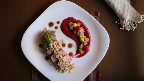 Ein kunstvoll angerichtetes Gourmetgericht mit Fleisch, Beerenpüree und bunten Beilagen auf einem weißen Teller.