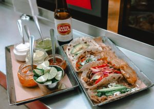 Ein Teller mit verschiedenen Tacos, Saucen und einer Flasche Carta Blanca Bier, ideal für mexikanische Küche.