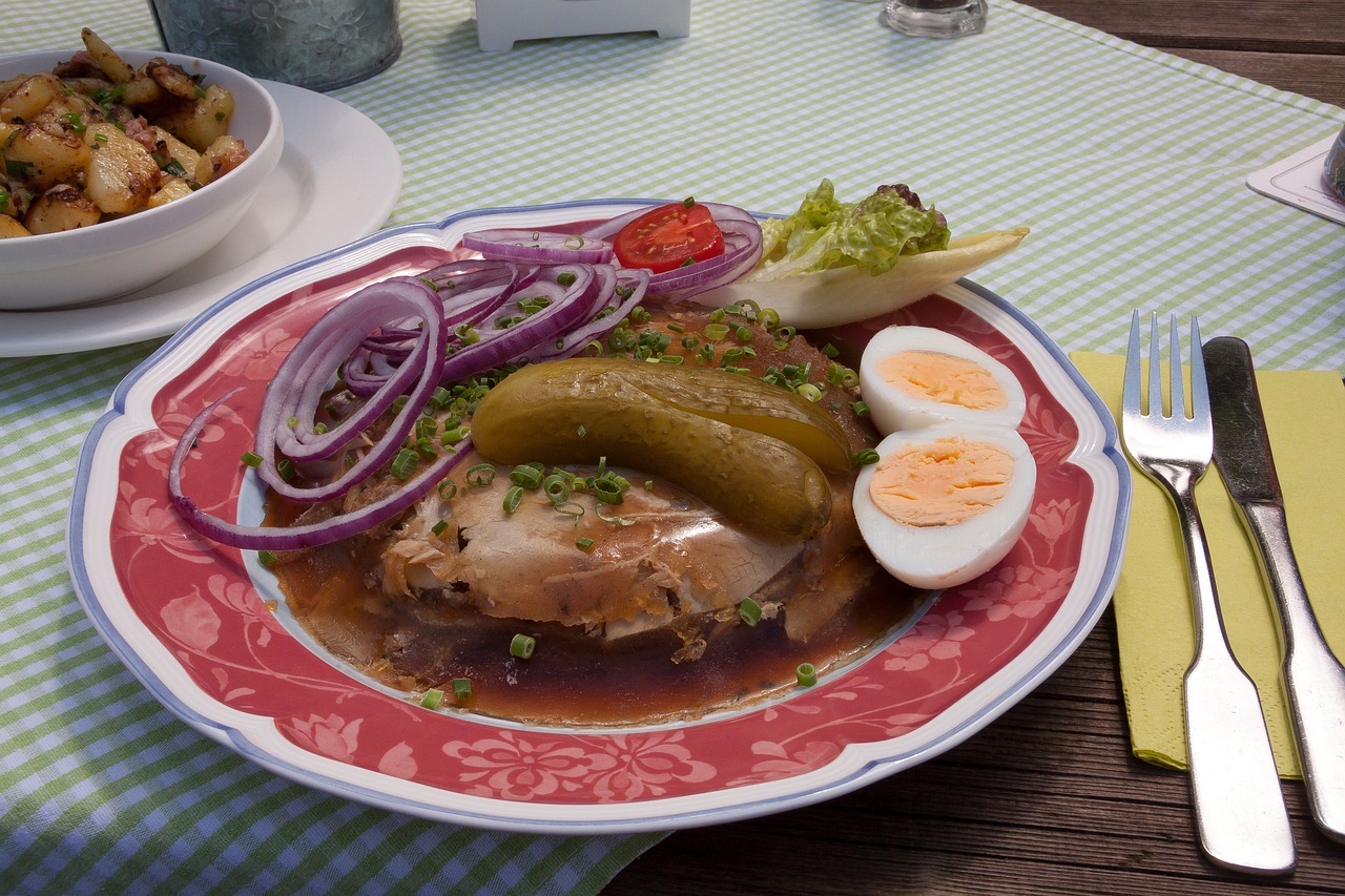 Ein Teller Sülze mit Fleisch, gekochten Eiern, Gewürzgurken, Zwiebeln und frischem Gemüse auf einem dekorativen Teller.