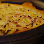 Leckerer Zwiebelkuchen mit Speckstücken, goldbraun gebacken, in einer runden Auflaufform. Perfekte Beilage für jedes Gericht.