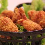 Frittierte Hähnchenflügel auf einem Bett aus frischem Salat in einem Korb, ideal für Snack- und Partygerichte.