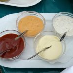 Vier verschiedene Dips in Schalen: Ketchup, Käse, Joghurt und Mayonnaise, serviert auf einem weißen Teller.