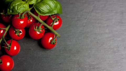 Eine Ansammlung von frischen Kirschtomaten mit grünen Basilikumblättern auf einem dunklen Hintergrund, ideal für kulinarische Anwendungen.