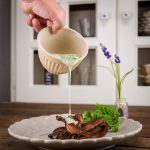 Gegrillte Pilze auf einem Teller mit einer cremigen Sauce Béarnaise, die aus einer Schüssel gegossen wird, garniert mit frischen Kräutern.