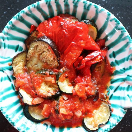 Ein Teller mit gebackenem Gemüse, darunter Zucchini, Auberginen und Paprika in Tomatensauce, serviert in einer dekorativen Schüssel.