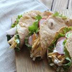 Gesunde Tacos gefüllt mit Fischfilet, Salat, Radieschen und Käse auf einem Holzbrett.