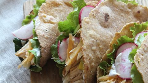 Gesunde Tacos gefüllt mit Fischfilet, Salat, Radieschen und Käse auf einem Holzbrett.