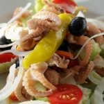 Frischer Meeresfrüchte-Salat mit Tintenfisch, Tomaten, Oliven und Zwiebeln auf einem Teller, gesund und schmackhaft.