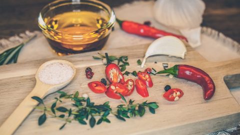 Frische rote Chilischoten, geschnitten mit Kräutern und Salz auf einem Holzbrett, begleitet von Öl und Zwiebel.