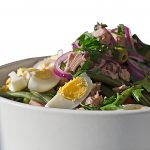 Bunter Salat mit gekochten Eiern, Thunfisch, grünen Bohnen und roten Zwiebeln in einer weißen Schüssel.