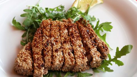 Sesamgebratener Thunfisch auf einem Bett aus frischem Rucola mit Zitronenscheibe, ideal für Feinschmecker und Liebhaber der asiatischen Küche.