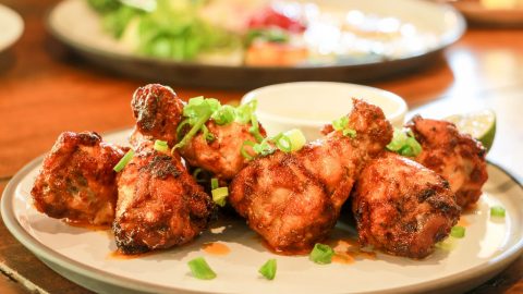 Gegrillte Hähnchenschenkel auf einem Teller mit Frühlingszwiebeln und Sauce, appetitlich angerichtet.