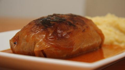 Ein gefüllter Kohl mit einer goldbraunen Kruste, serviert mit cremigem Kartoffelpüree auf einem weißen Teller.