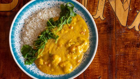 Ein Teller mit Curry, Reis und frischem Spinat auf einem rustikalen Holztisch. Leckeres Gericht mit aromatischen Zutaten.