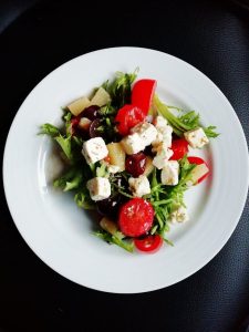Bunter Salat mit Feta, Tomaten, Paprika und grünen Blättern auf einem weißen Teller, ideal für gesunde Ernährung.