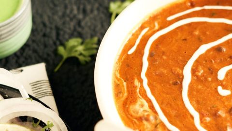 Ein Teller mit indischem Gericht in Soße, garniert mit Sahne, umgeben von Beilagen wie Zwiebeln und Saucen.