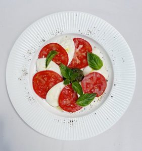 Frischer Caprese-Salat mit Mozzarella, Tomaten und Basilikum auf einem weißen Teller, ideal für gesunde Ernährung.