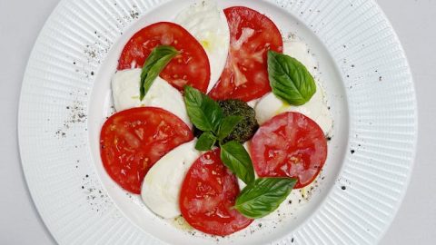Frischer Caprese-Salat mit Mozzarella, Tomaten und Basilikum auf einem weißen Teller, ideal für gesunde Ernährung.
