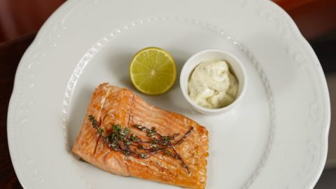 Gegrilltes Lachsfilet auf einem weißen Teller mit Limettenscheibe und einer Portion Sauce, ideal für Feinschmecker und Fischliebhaber.