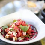 Ein frischer Salat mit Wassermelonenstücken, Feta-Käse, Kräutern und einer bunten Beetroot-Sauce in einer eleganten Schüssel.
