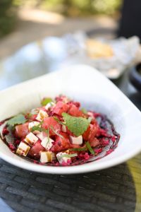 Ein frischer Salat mit Wassermelonenstücken, Feta-Käse, Kräutern und einer bunten Beetroot-Sauce in einer eleganten Schüssel.