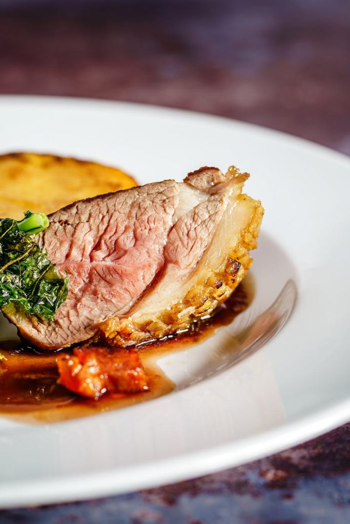 Ente a l'orange, perfekt gegart, serviert mit Gemüse und einer köstlichen Sauce auf einem weißen Teller.